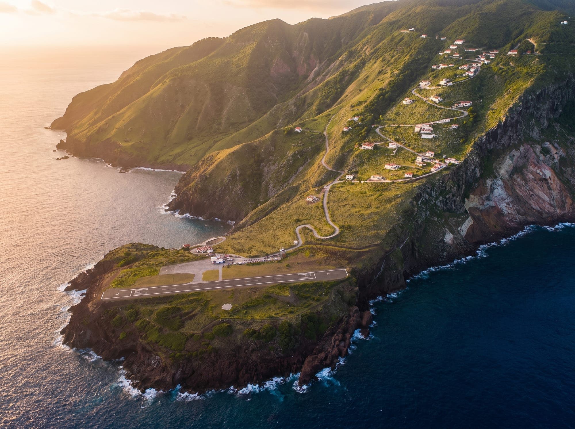 Saba's airport runway on the cliff edge at sunset, with the switchback road climbing the mountain above it